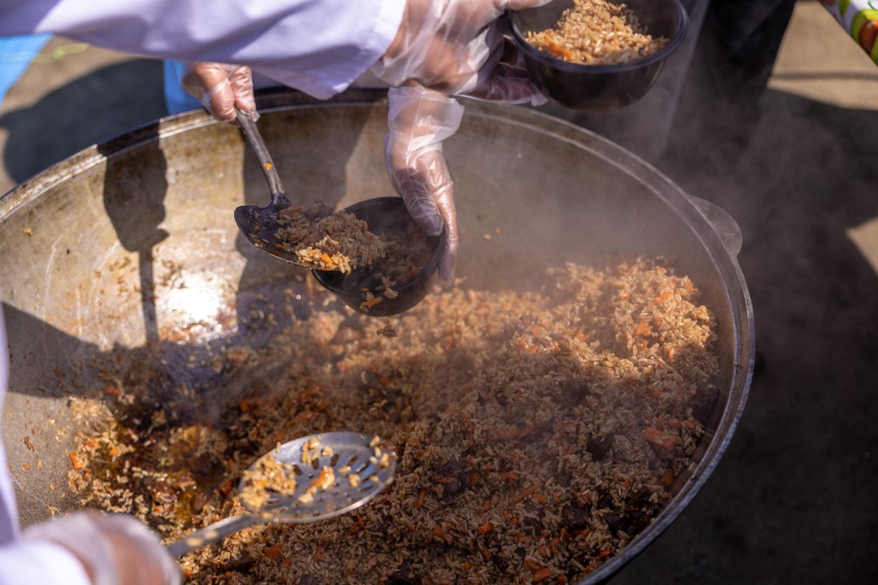 Hands scoop rice dish into bowls, showcasing vibrant street food preparation.
